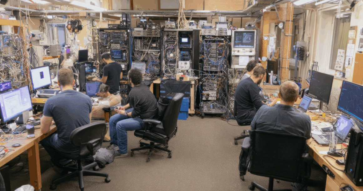 Engineers working in a hardware lab surrounded by servers, cables, and real-time simulation equipment.