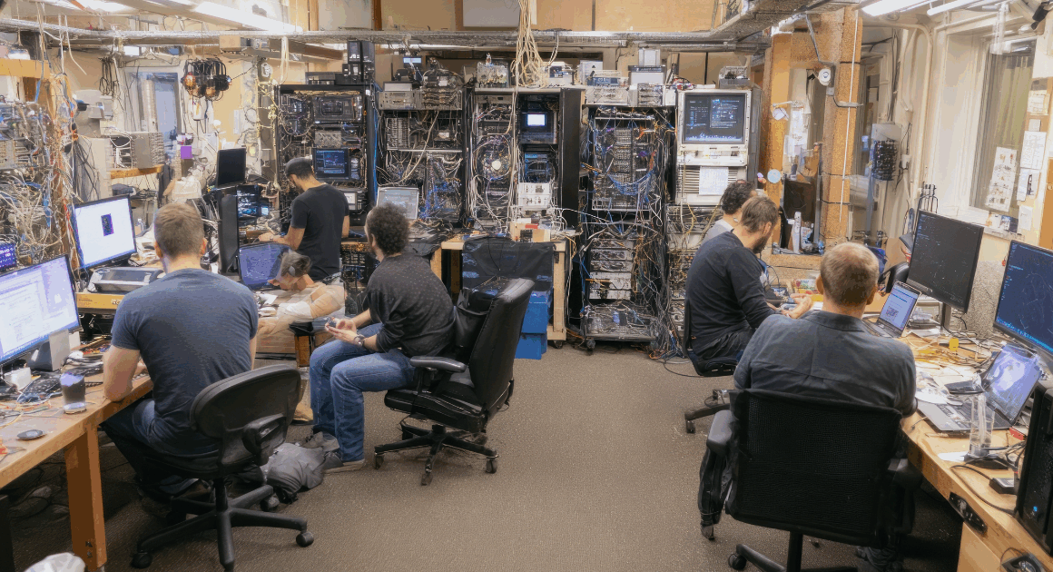 Engineers working in a hardware lab surrounded by servers, cables, and real-time simulation equipment.